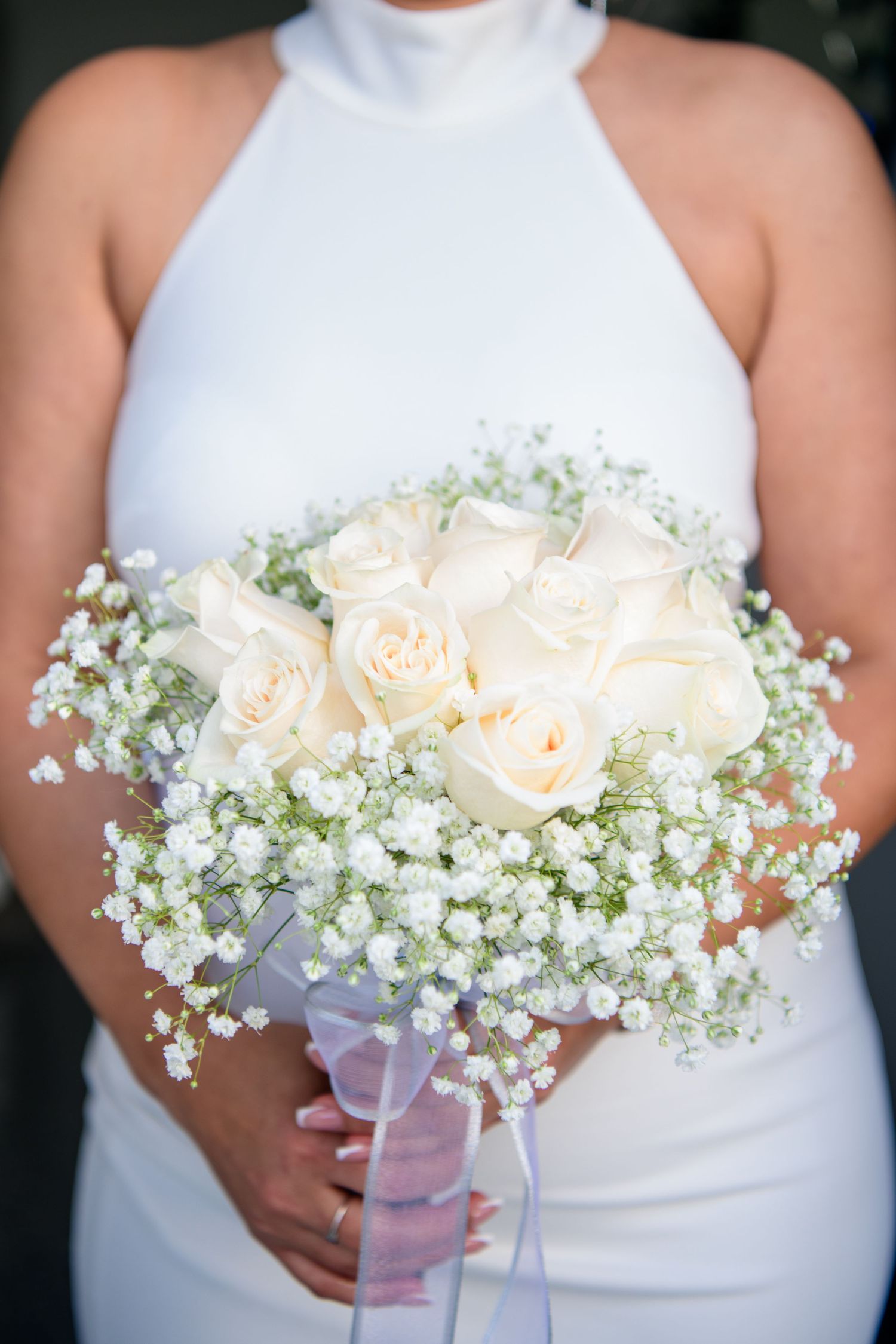 Wedding portrait of bouquet featuring cream roses and baby's breath flowers with white ribbon wrap.