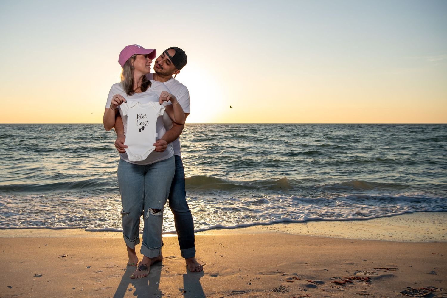 A loving couple shares an intimate moment on the beach with the ocean and setting sun behind them. Maternity photoshoot. Couples photos.