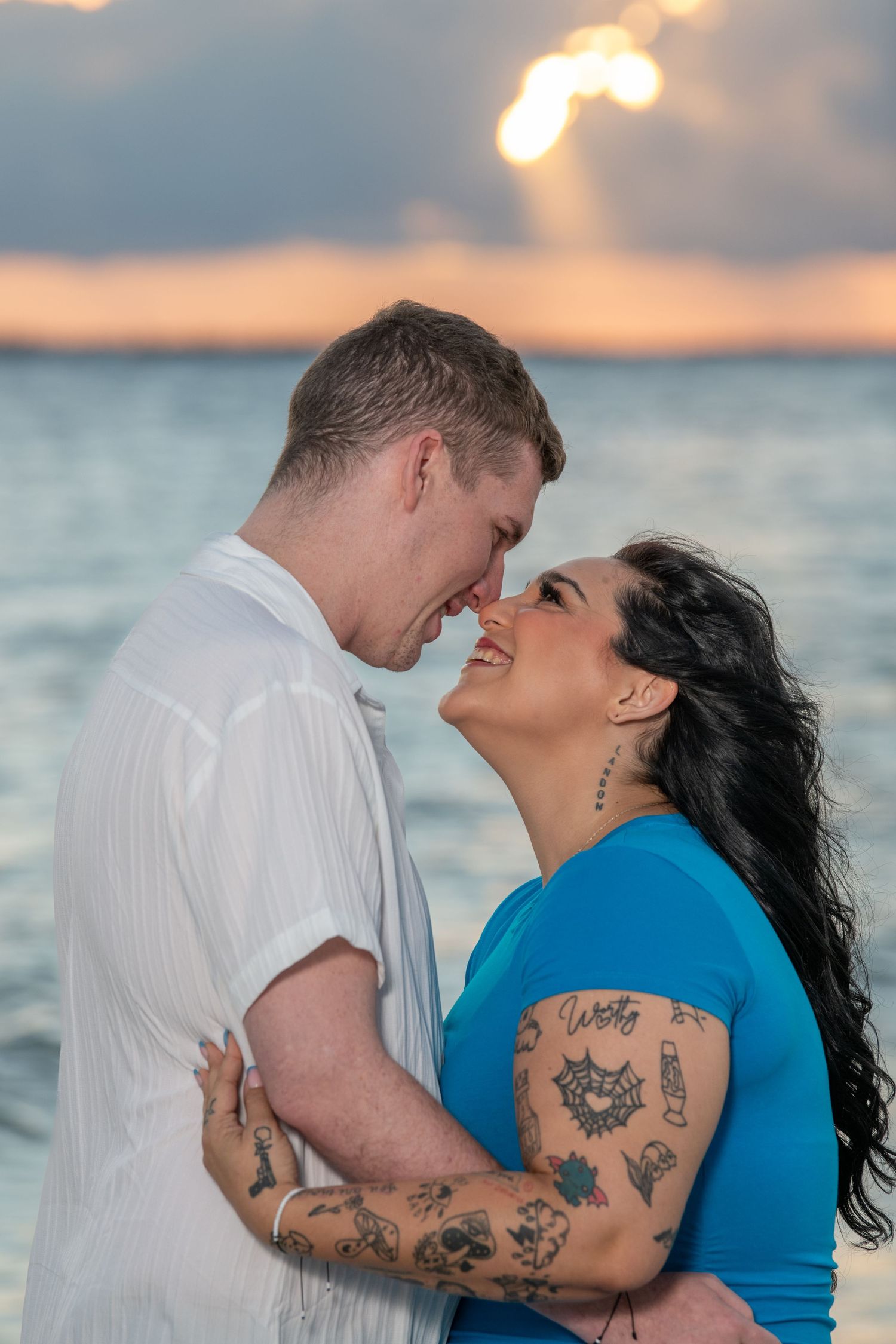 A couple shares a joyful moment together against a dramatic sunset beach backdrop.