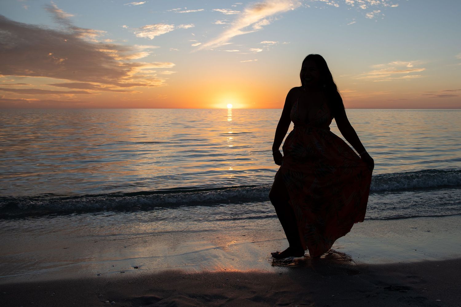Silhouette of person in flowing dress against dramatic beach sunset. Beach photoshoot.