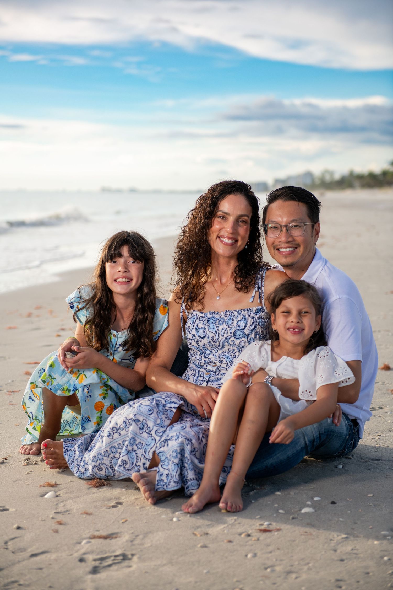A family of four sits together on a sunny beach wearing coordinated blue and white outfits.