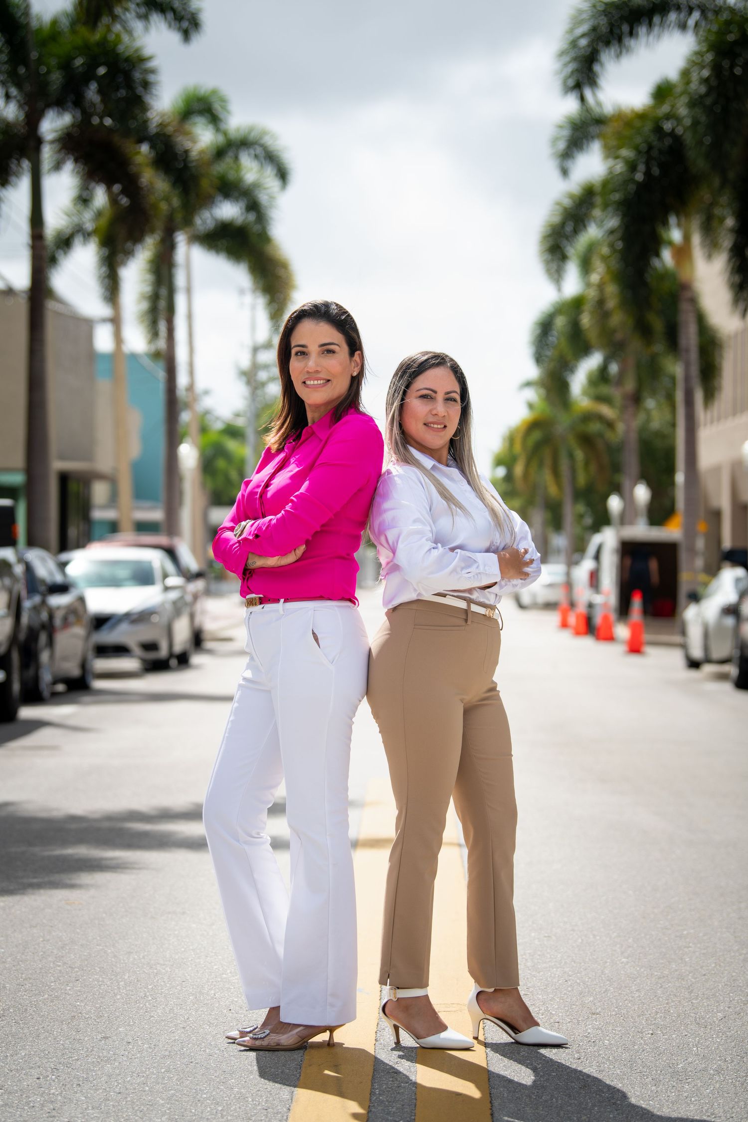 Two business professionals posing playfully on a palm-lined street.
