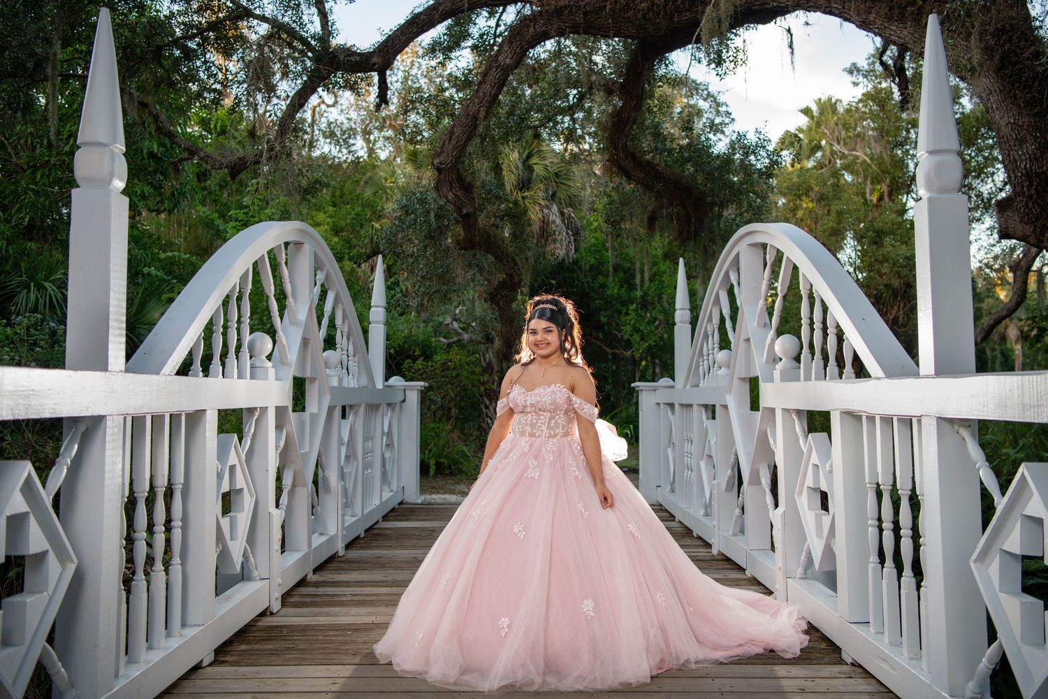 Flowing pink ballgown captured on a white wooden bridge surrounded by greenery. Quinceañera photos.