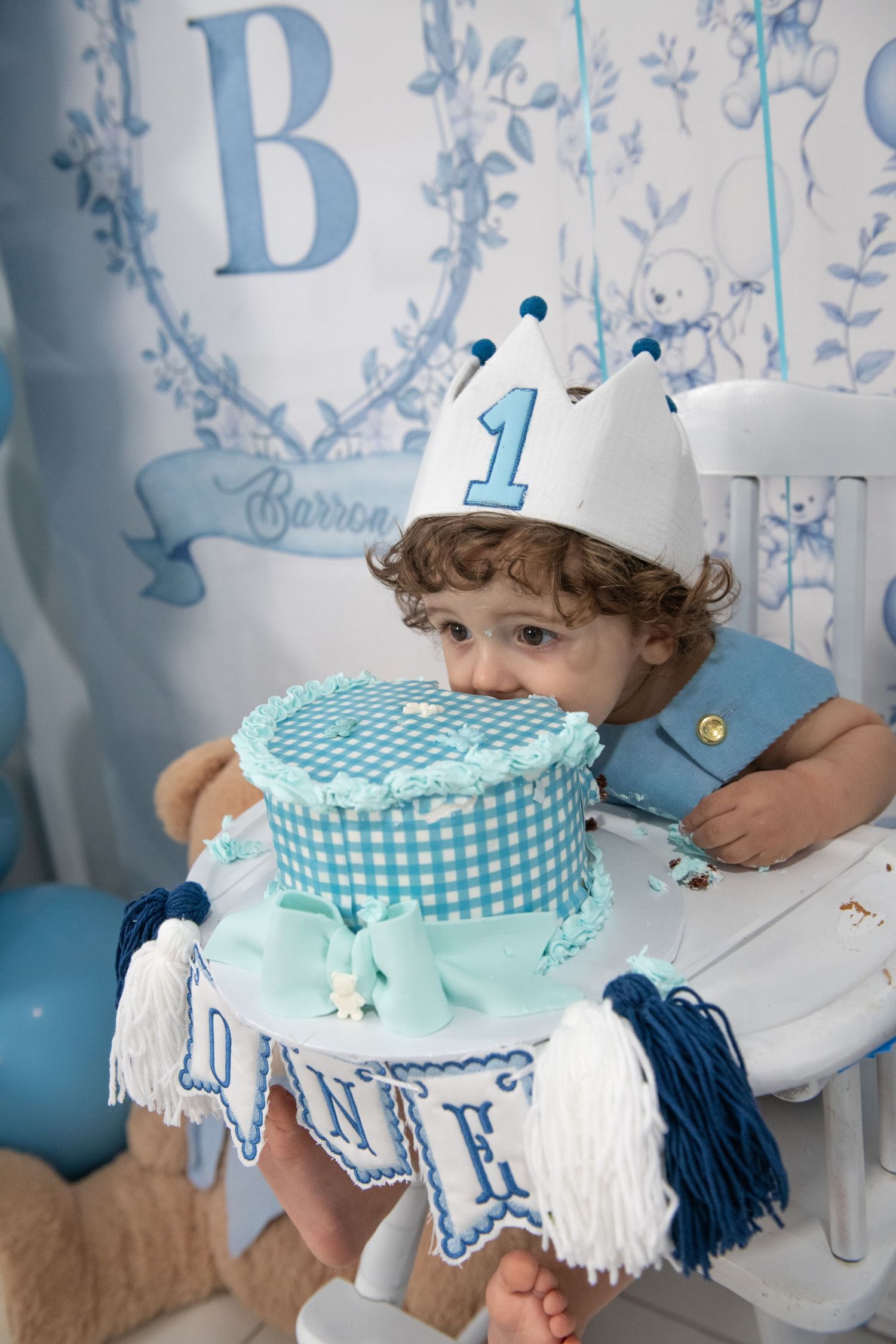 Blue and white themed first birthday party setup with a gingham cake and decorative banner.