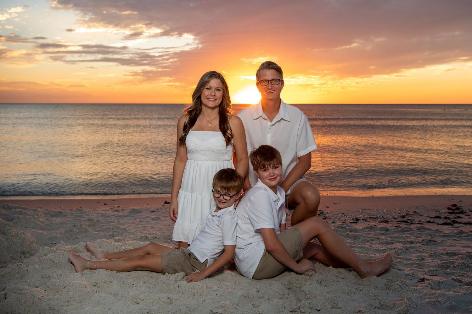 A group relaxing together on a sandy beach during a vibrant orange sunset over the ocean. Beach photoshoot. Family photoshoot,