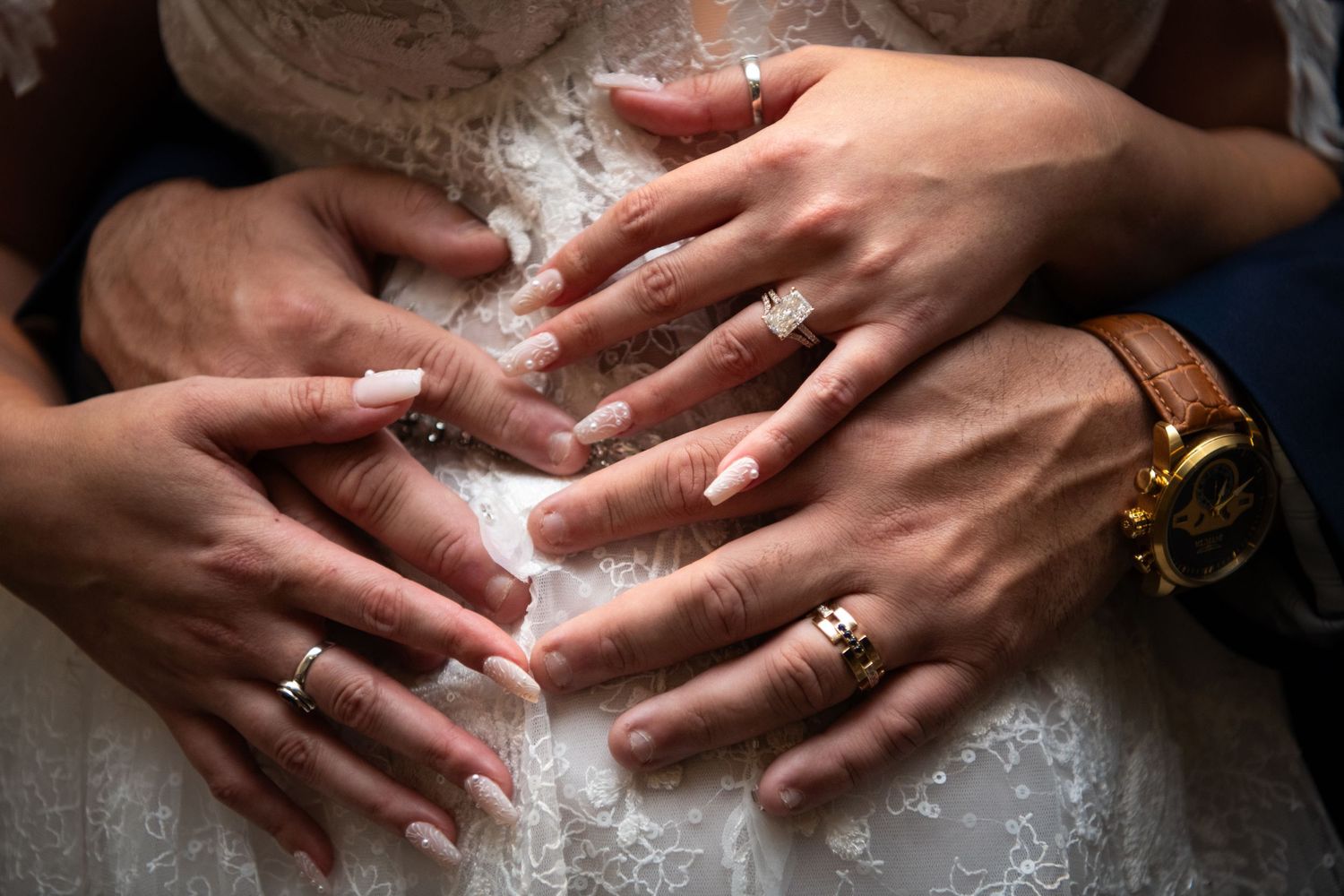 Close-up of hands displaying wedding rings against white lace dress fabric.