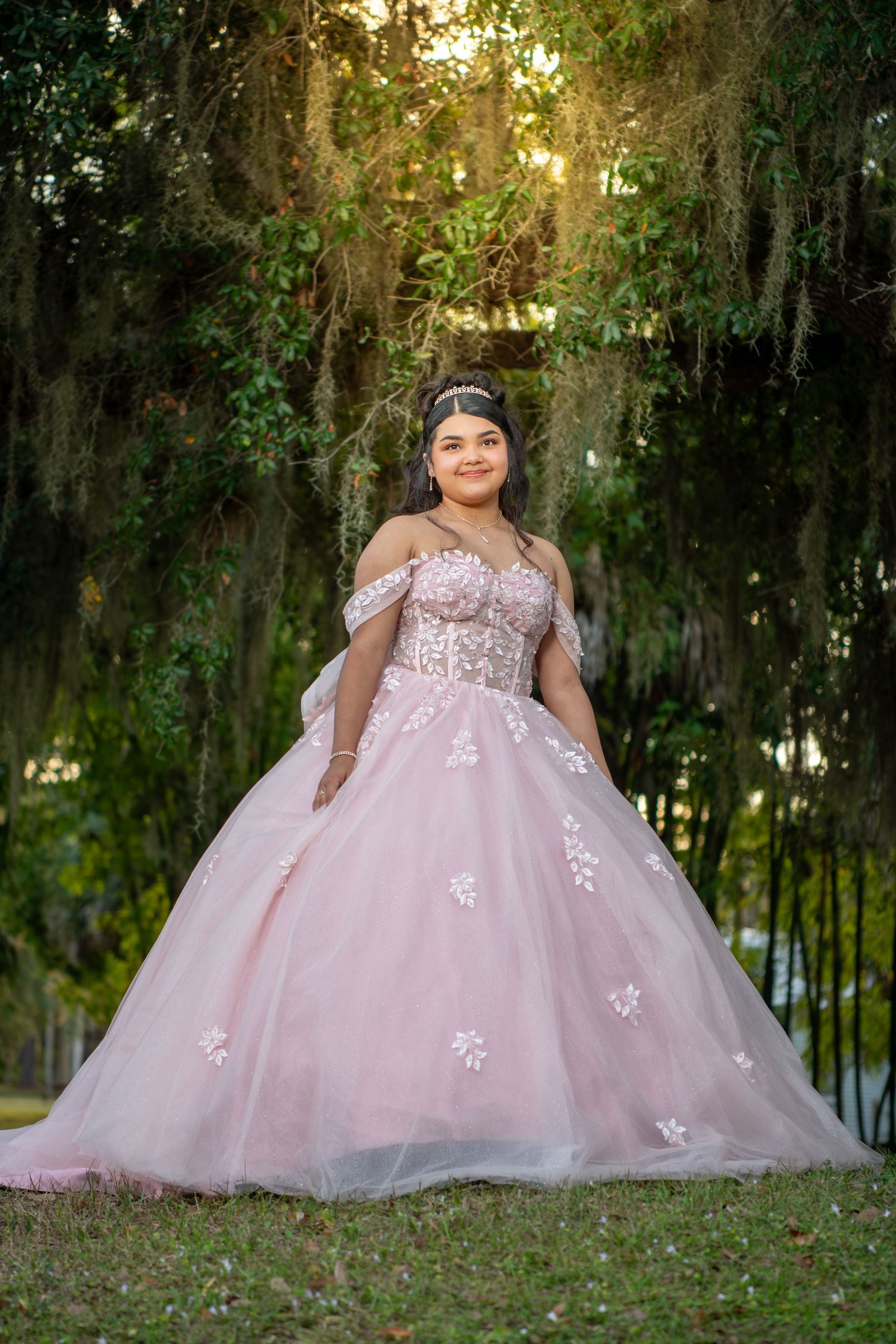 A pink princess ball gown with lace details photographed in a mossy garden setting.Quinceañera photos.