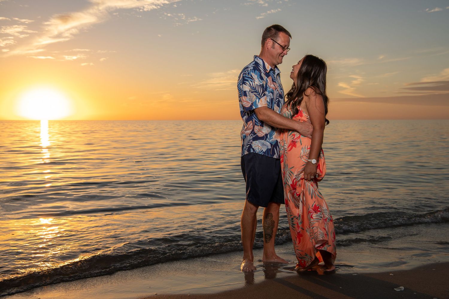 Couple embracing on beach with dramatic orange sunset over calm ocean waters. Beach photoshoot. Family photoshoot,
