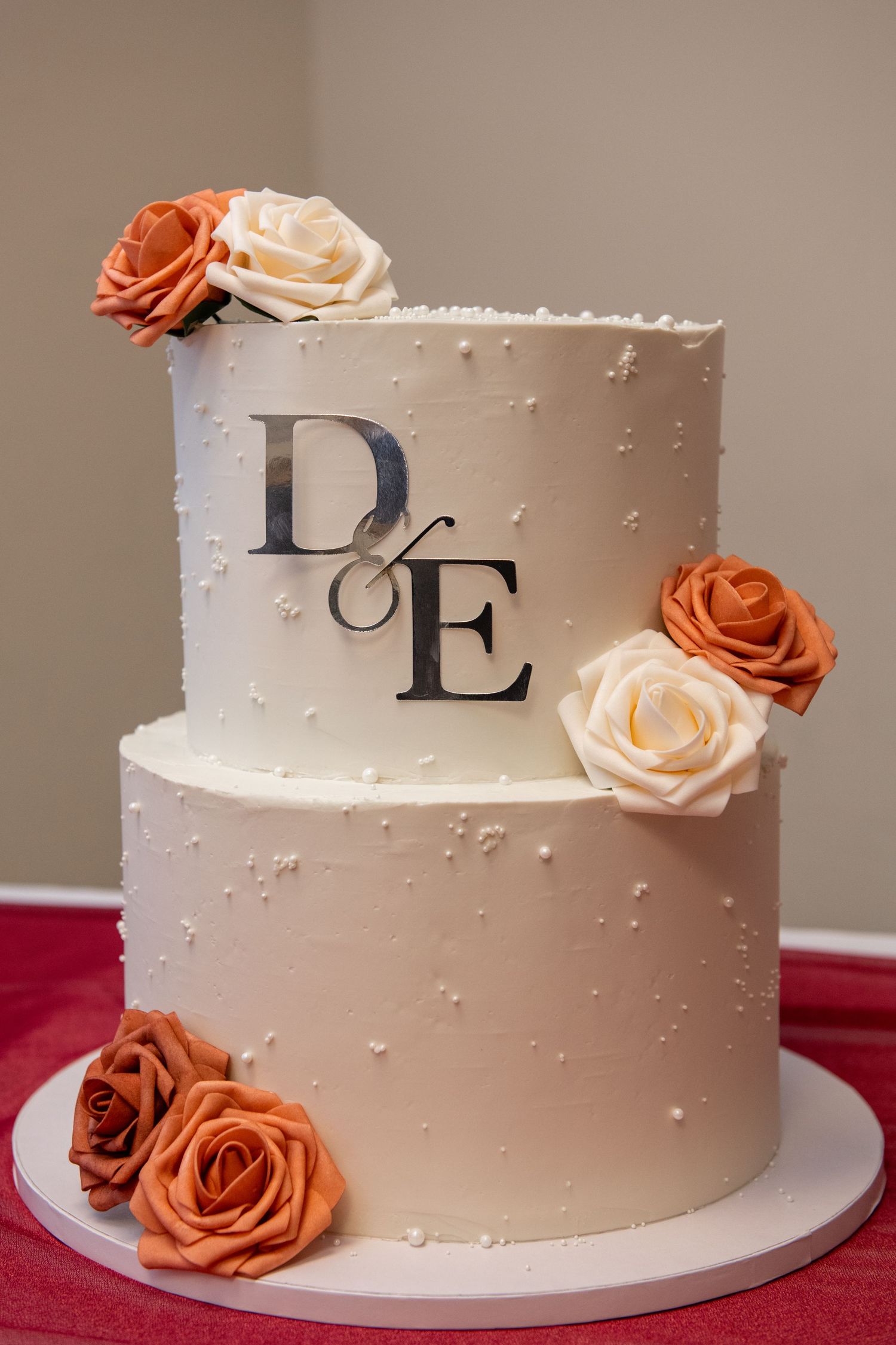 Elegant white wedding cake decorated with orange and cream roses and monogram letters.