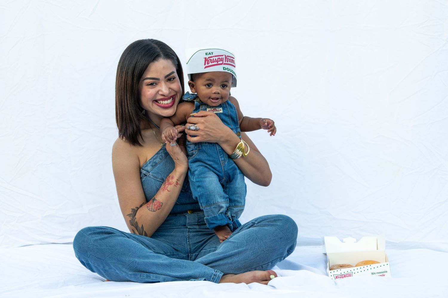 Baby in denim plays while being held on white background.