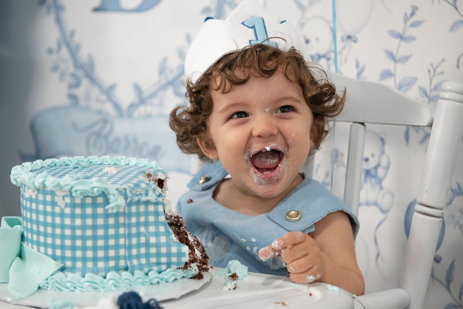 A festive first birthday party scene with blue and white decorations and a gingham cake.