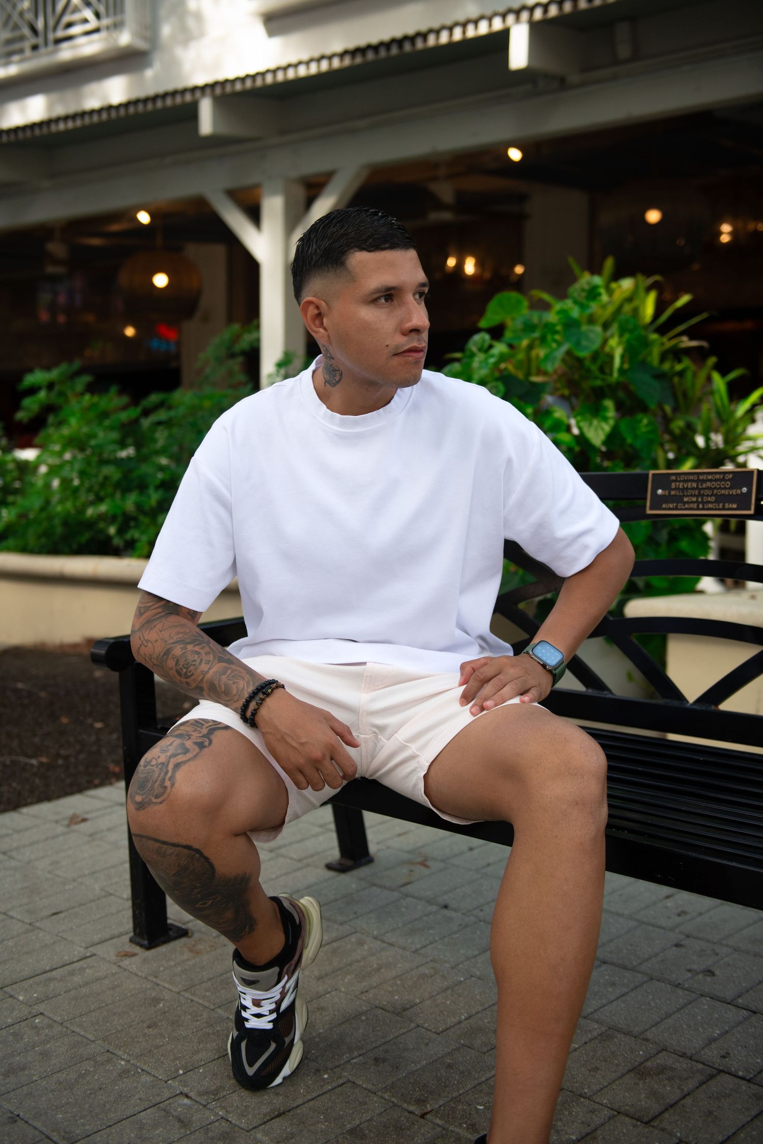 Athletic summer style with white t-shirt and shorts sitting on outdoor bench with urban backdrop.