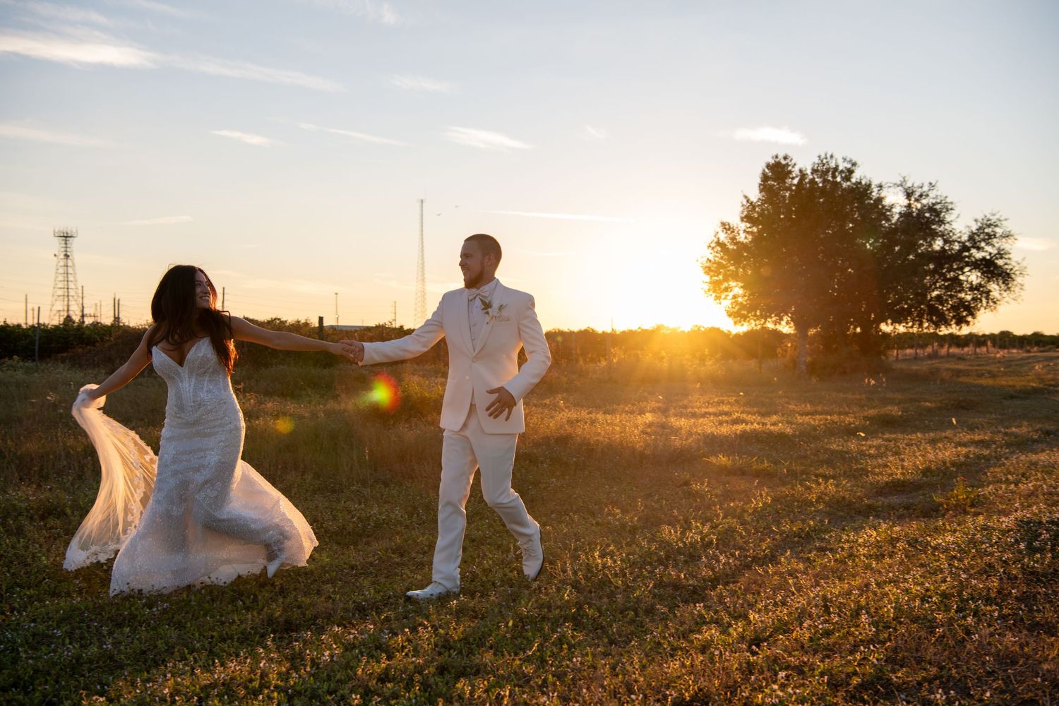 Wedding couple poses playfully in a grassy field during sunset photography session. Wedding photography.
