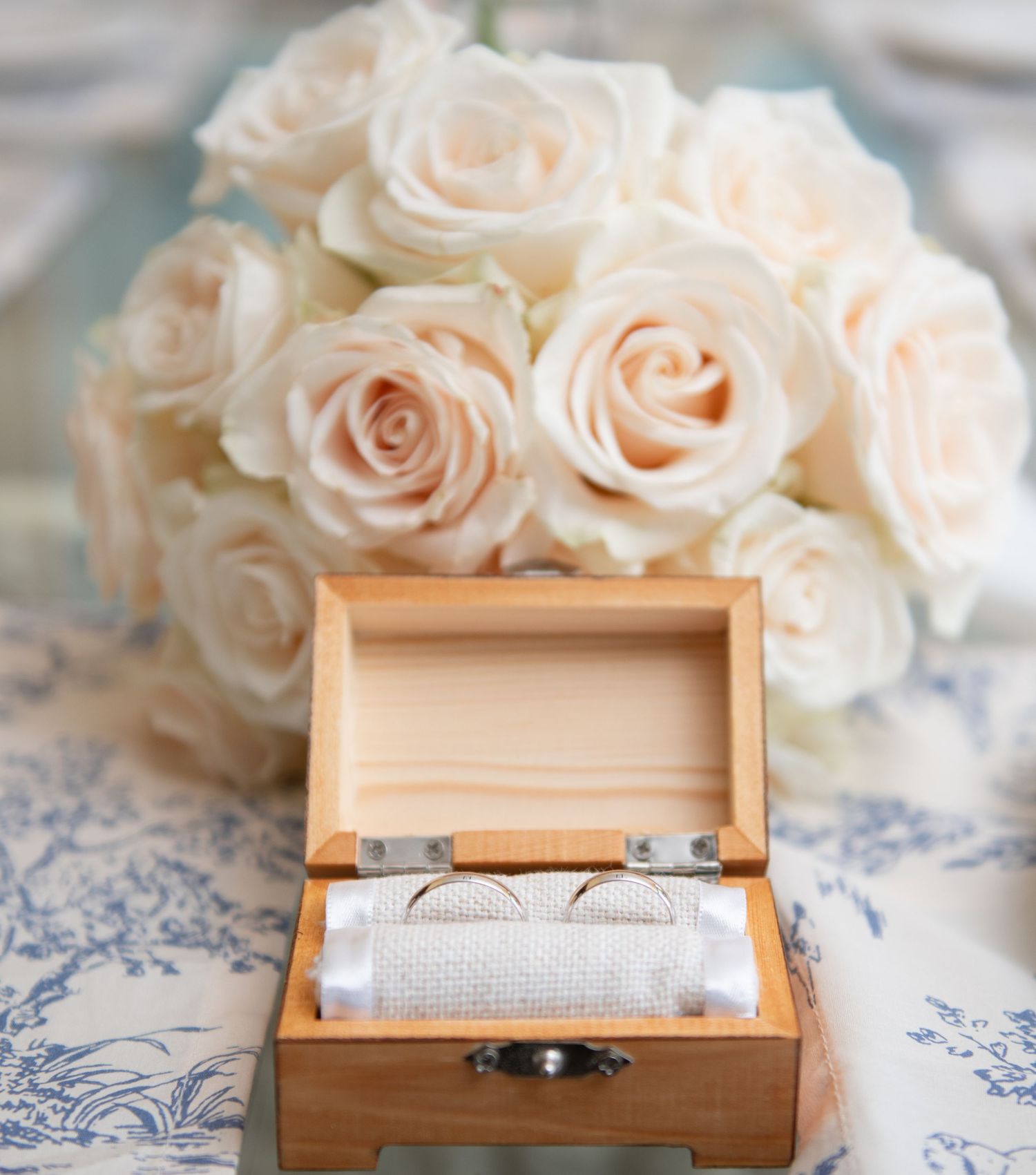 Wooden ring box with roses displayed on blue and white patterned fabric.