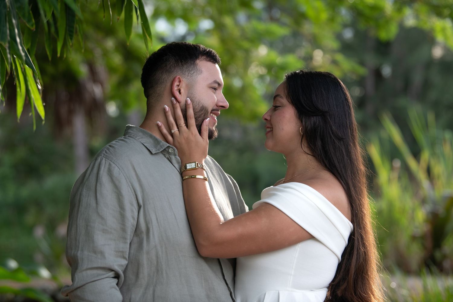 A couple embraces tenderly against a backdrop of green foliage in an outdoor setting.