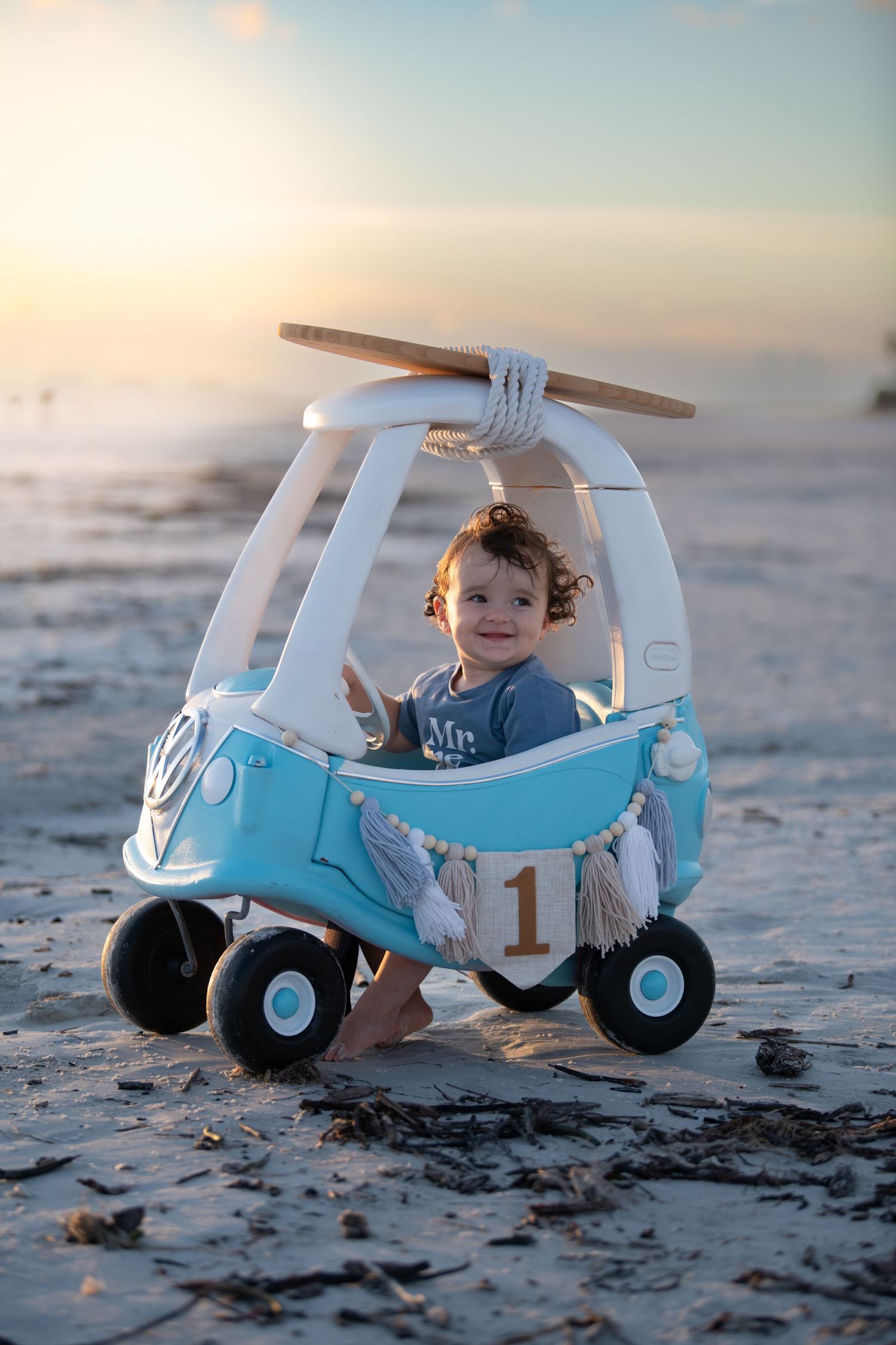A light blue toy car photographed on a sandy beach at sunset.