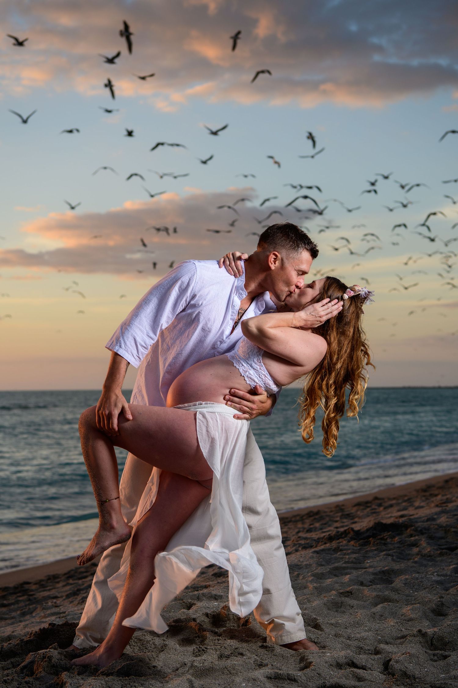 Dramatic dance dip pose on beach with seabirds flying in sunset sky. Maternity photoshoot,