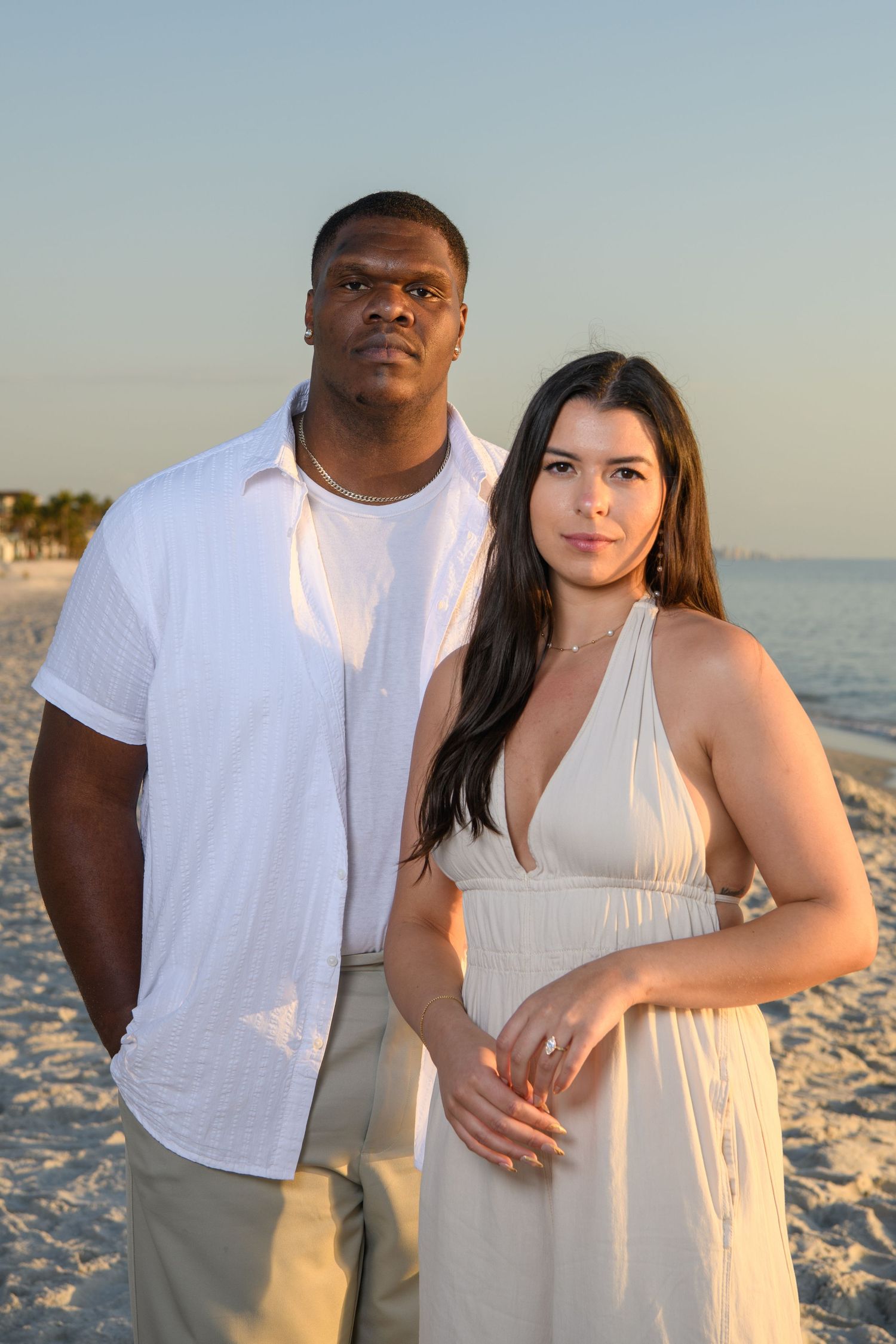 A couple poses together on a beach in white outfits during a sunset photoshoot. Engagement photoshoot. Couples photos.