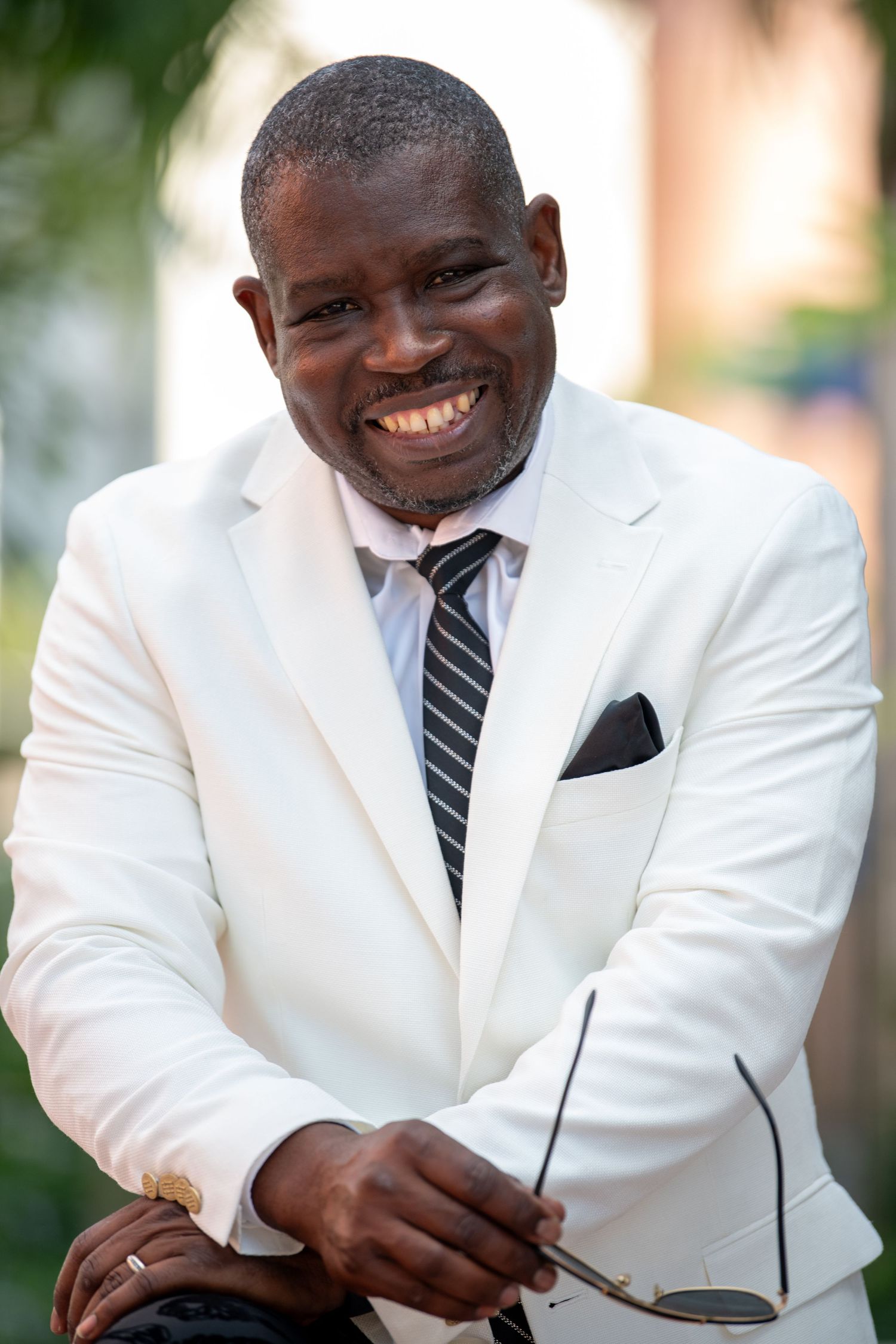 Professional portrait of someone in a crisp white suit jacket and striped tie showing a warm smile.