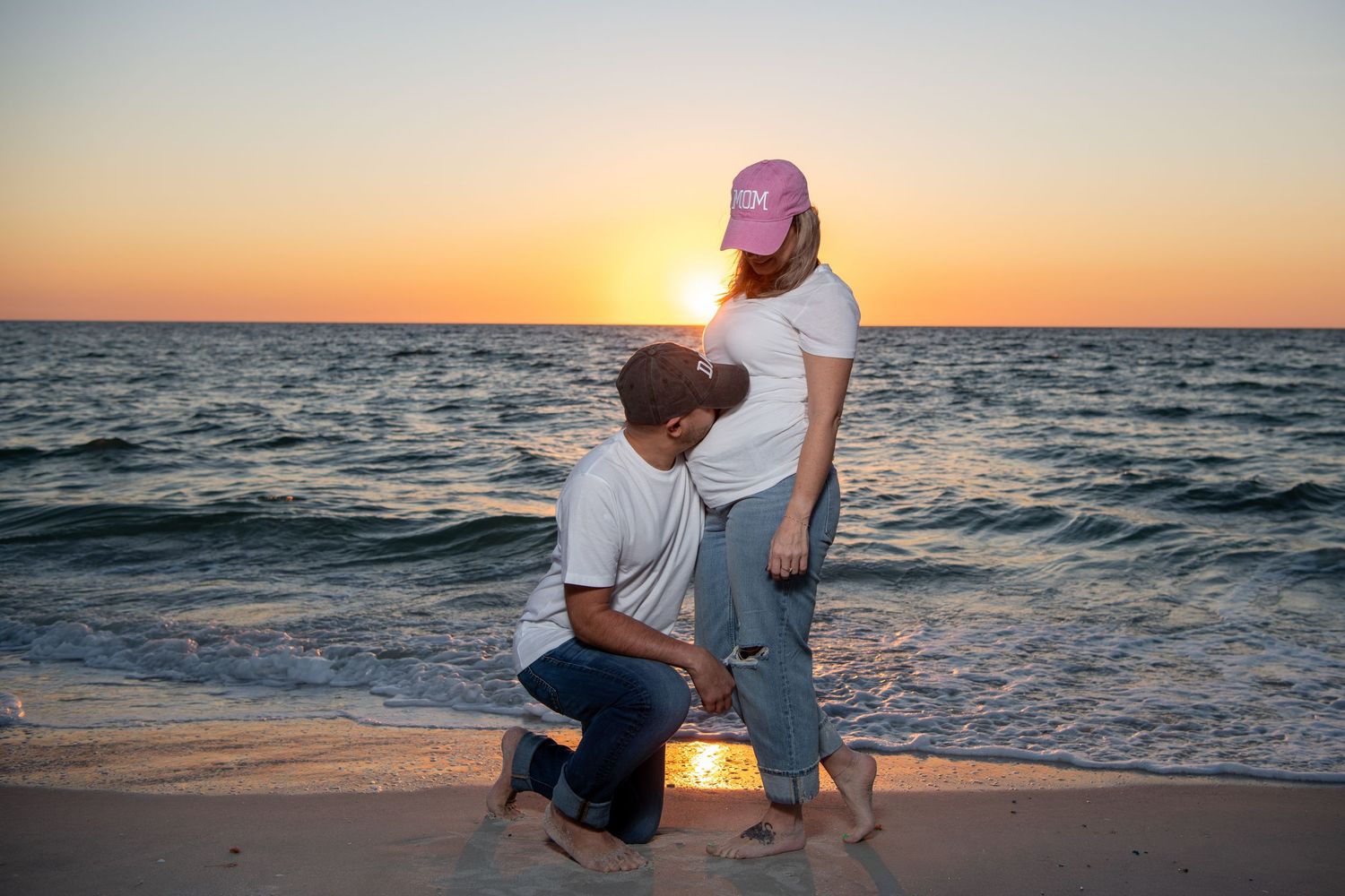 A sunset beach maternity photo showing a tender moment between expectant parents near the ocean waves. Maternity photoshoot. Couples photos.
