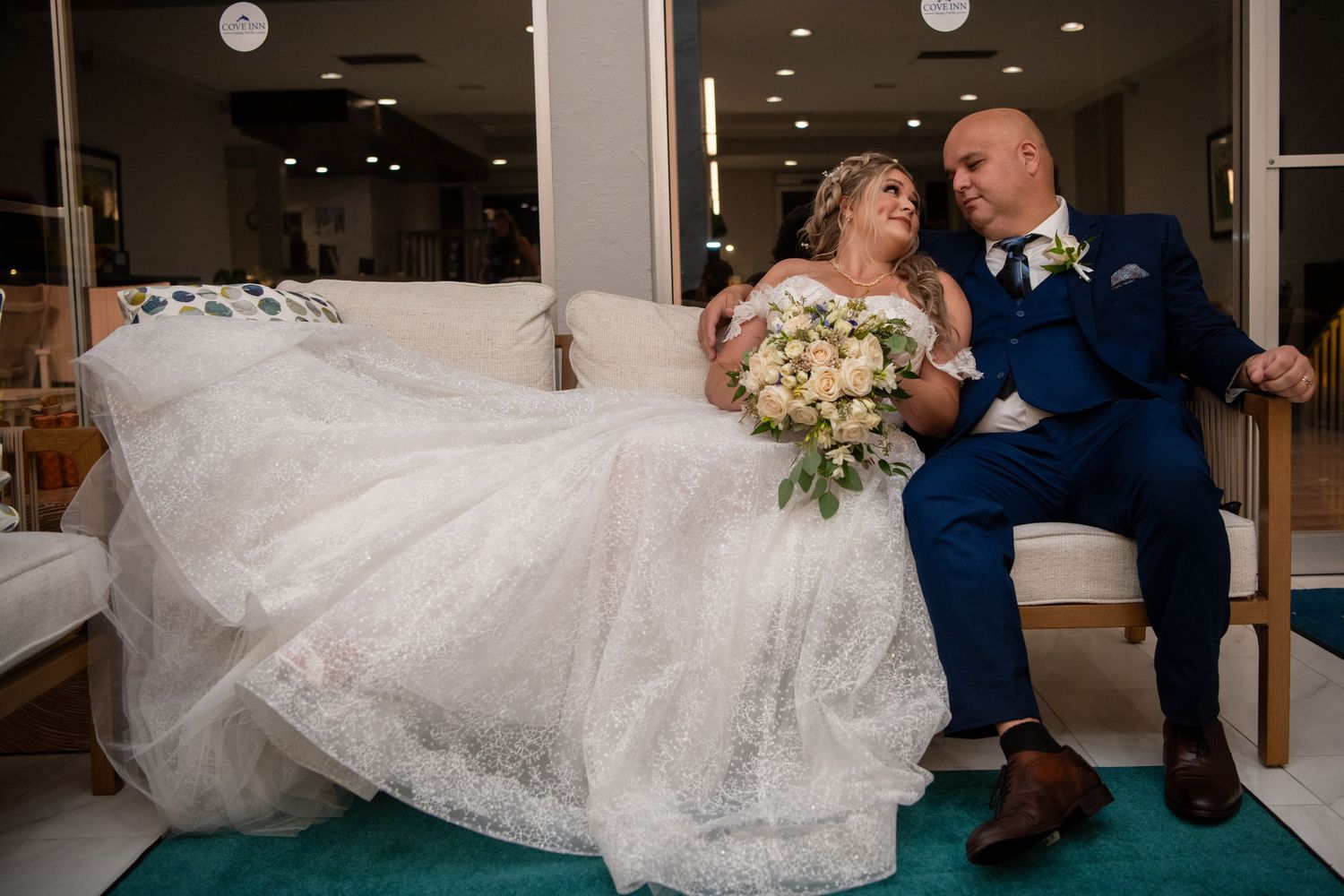 A couple sits together on a bench in an indoor venue with modern lighting.