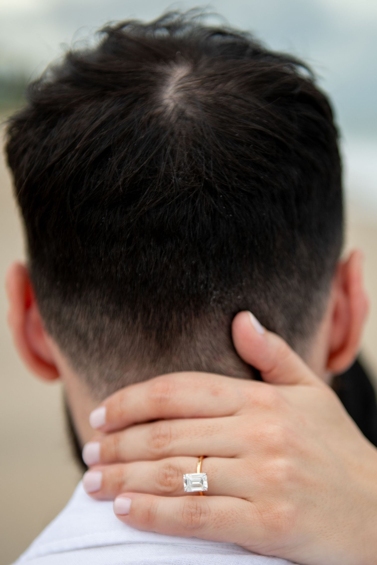 Close-up shot showing hands with an engagement ring against dark hair.