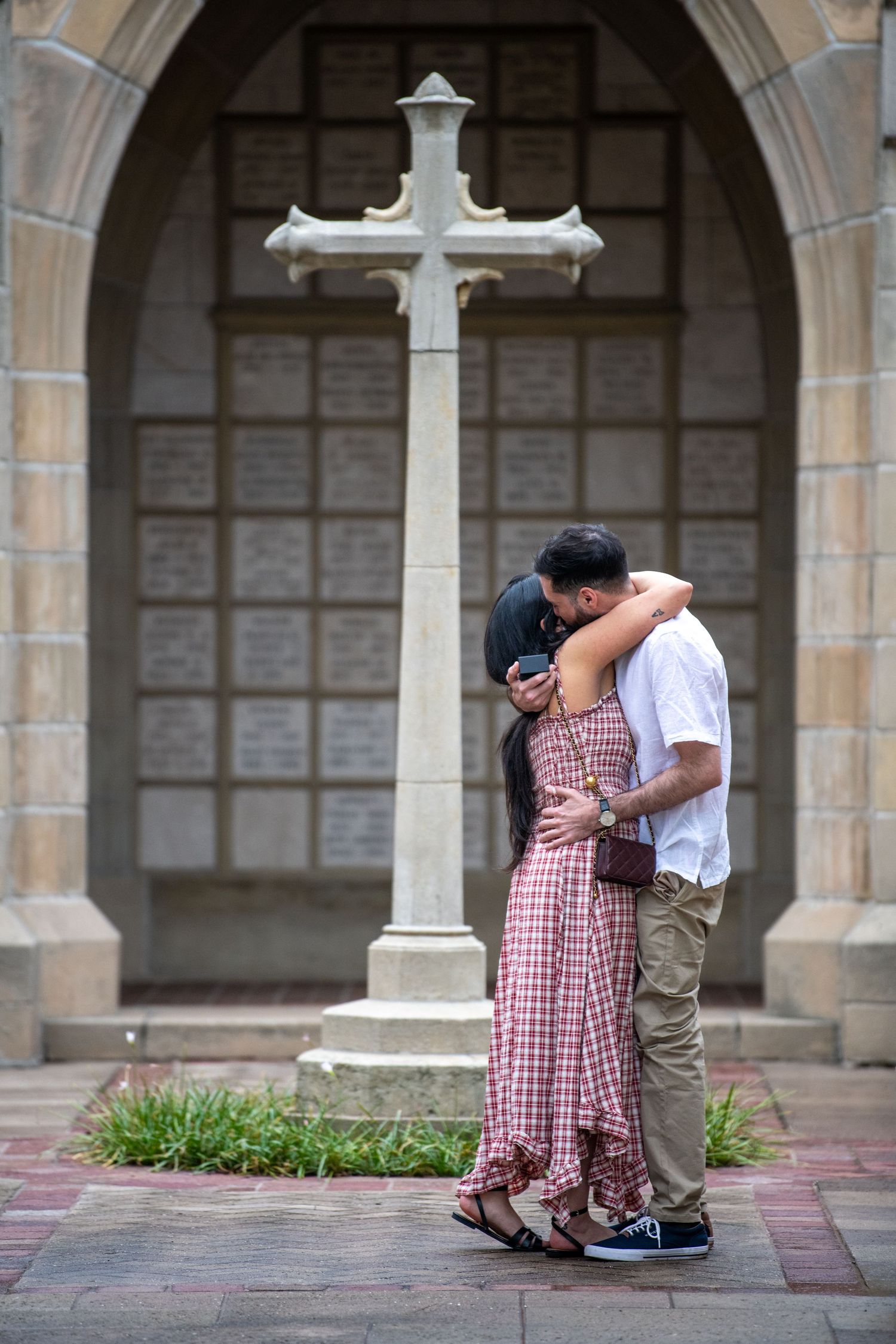 Couple sharing a tender moment in front of a stone church archway with crosses.
