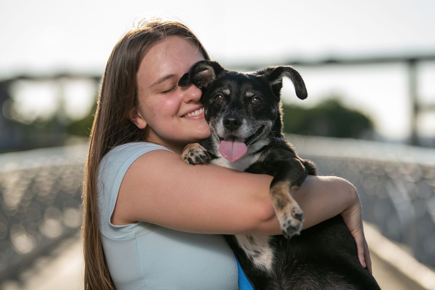 A person hugs and cuddles with their black and white dog on a bridge walkway. Dog portraits. Self portraits.