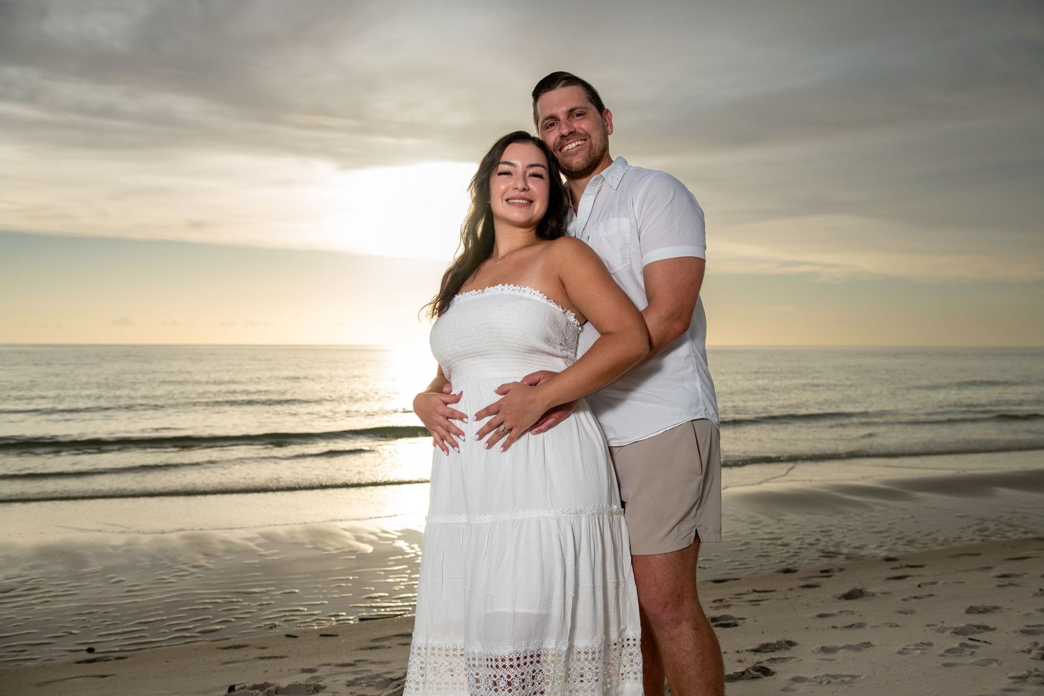 Couple embracing on beach at golden hour with ocean waves in background.