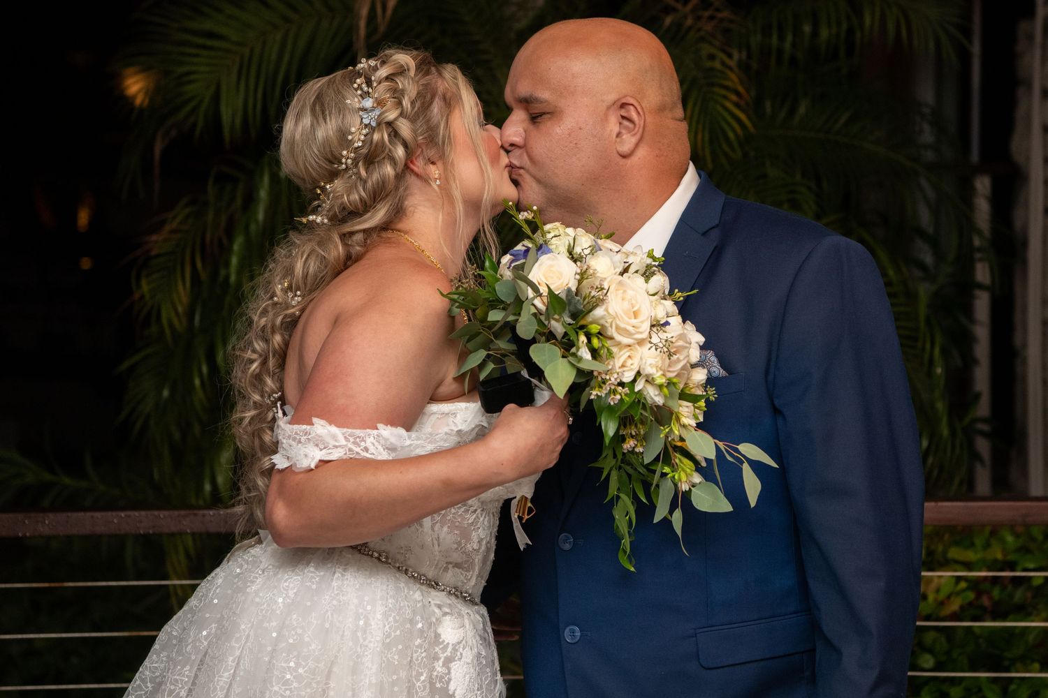 A couple embraces during their wedding ceremony while holding a white floral bouquet.
