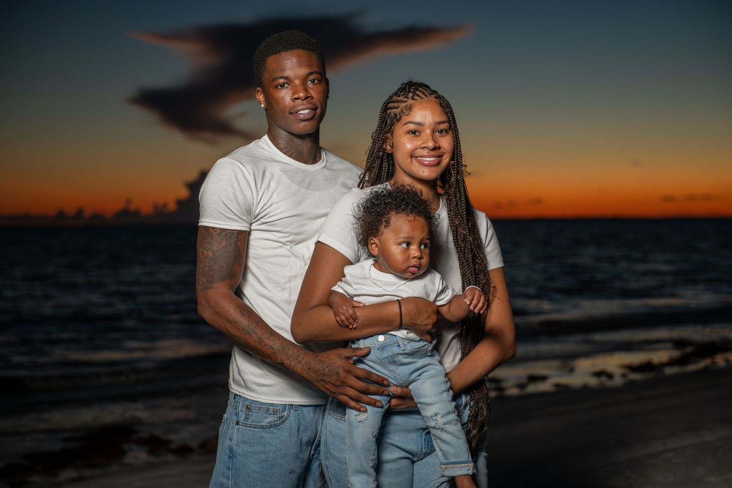 Family silhouettes against a vibrant orange sunset sky at the beach.