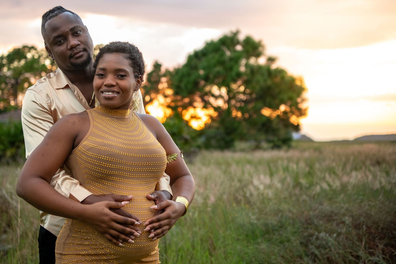 Couple embracing in golden field during sunset maternity photoshoot. Maternity photoshoot.