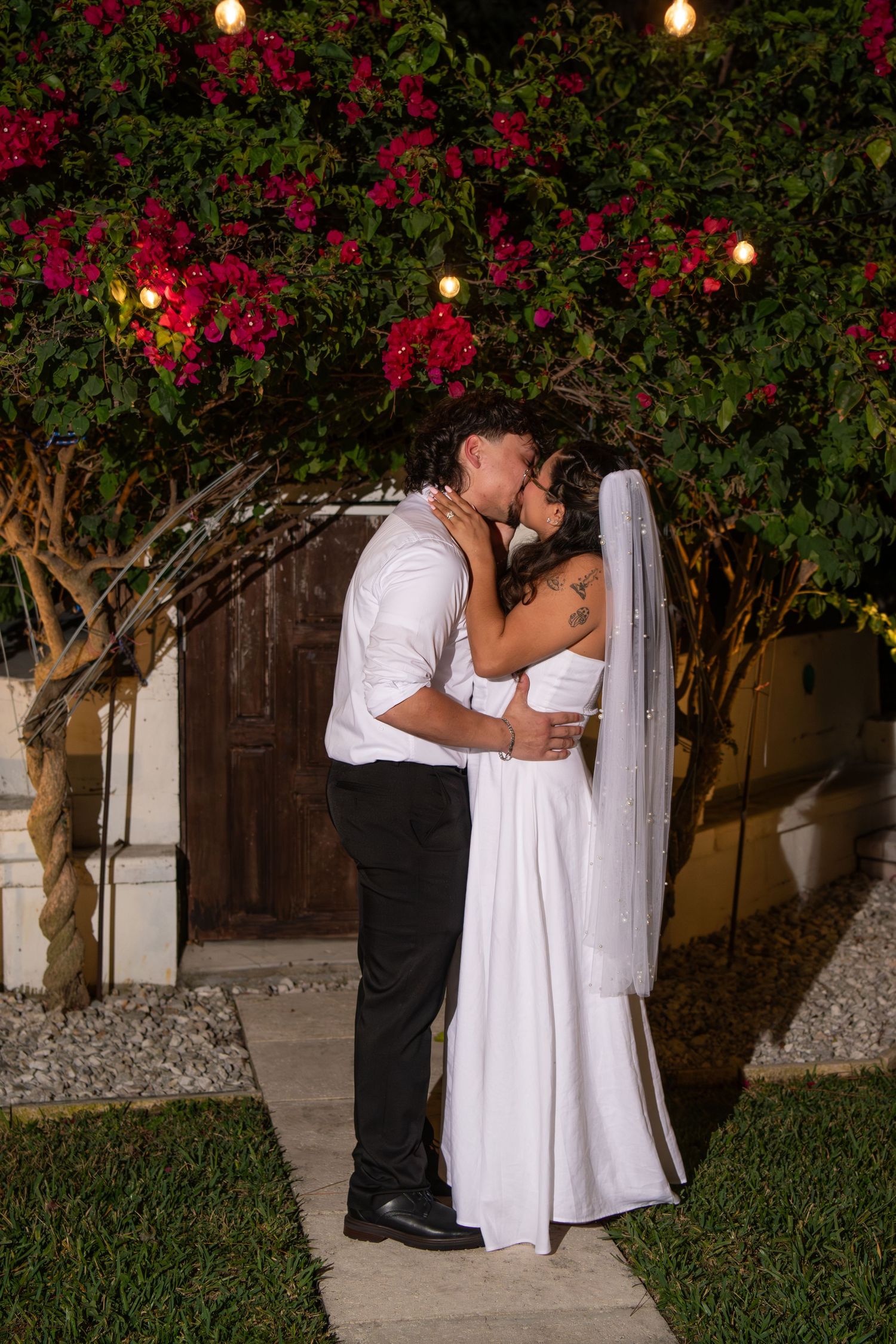 Wedding couple sharing romantic moment under flowering trees with string lights. Wedding photography.