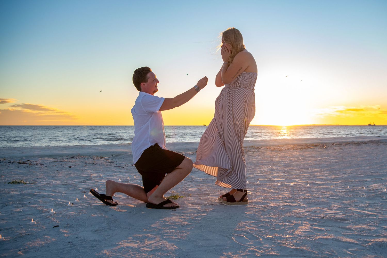 Couple on white sandy beach during golden hour with ocean waves in the background.