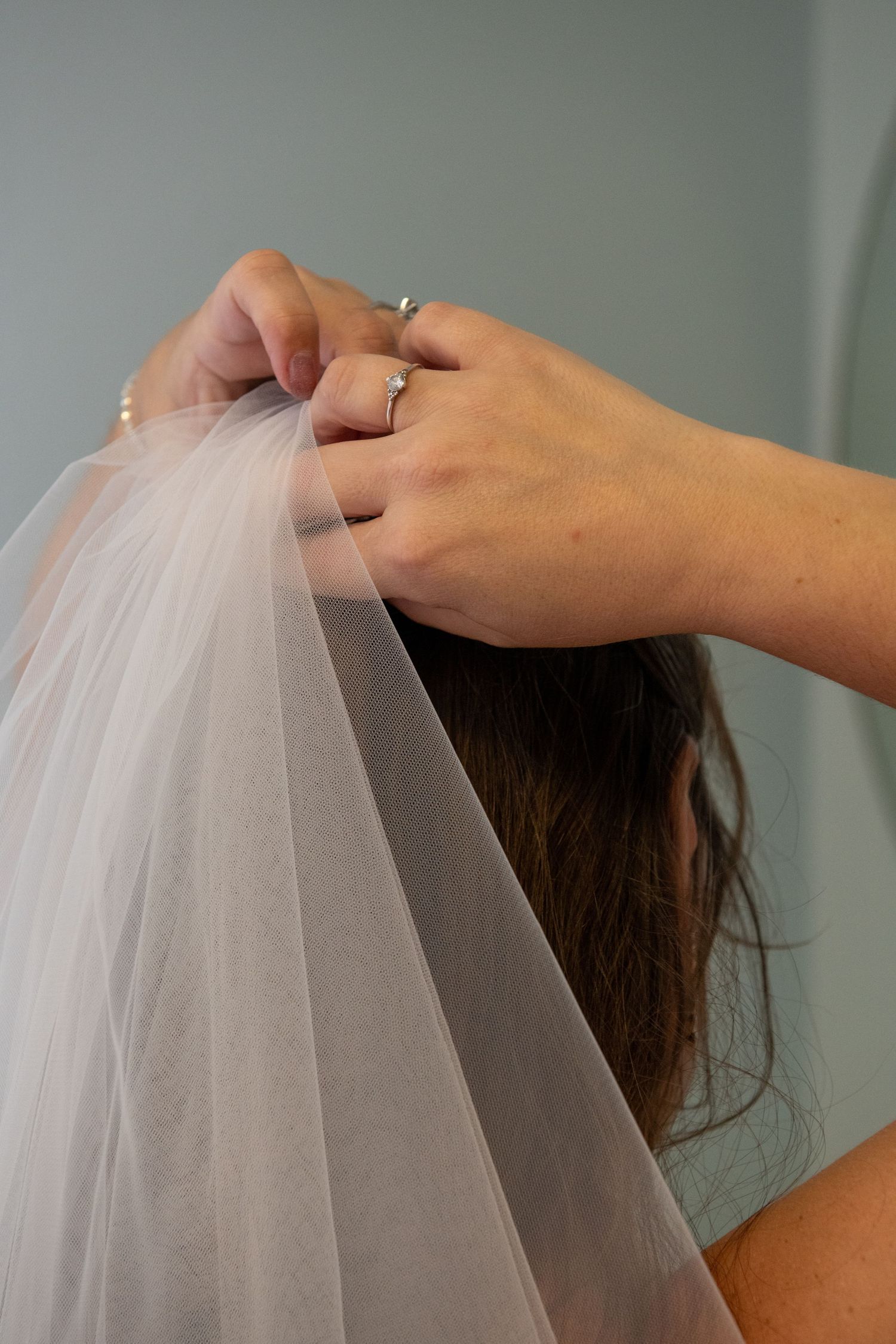 Hands adjusting a delicate white bridal veil during wedding preparations.