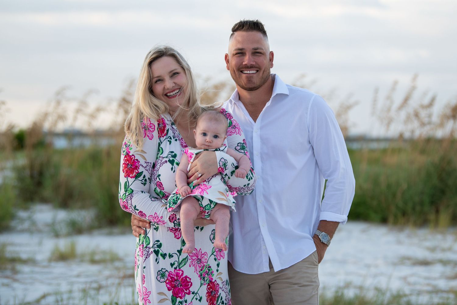 A family poses together on a beach with sea oats and coastal vegetation in the background at sunset.