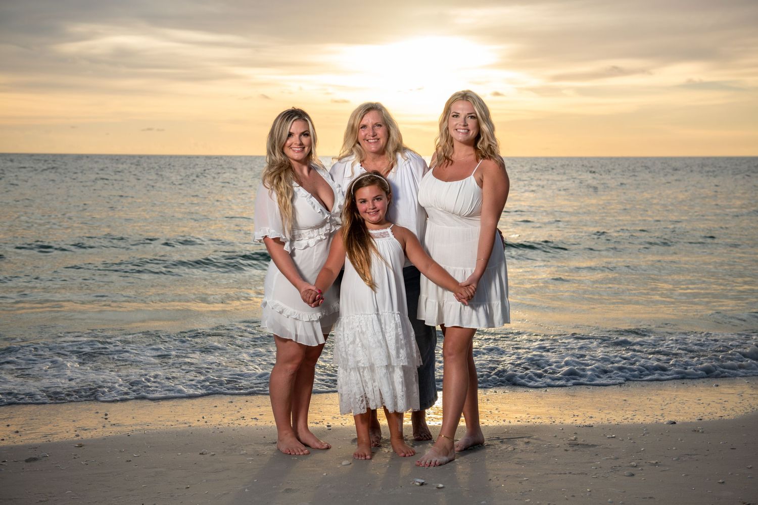 Family members in white outfits pose together on beach at sunset.