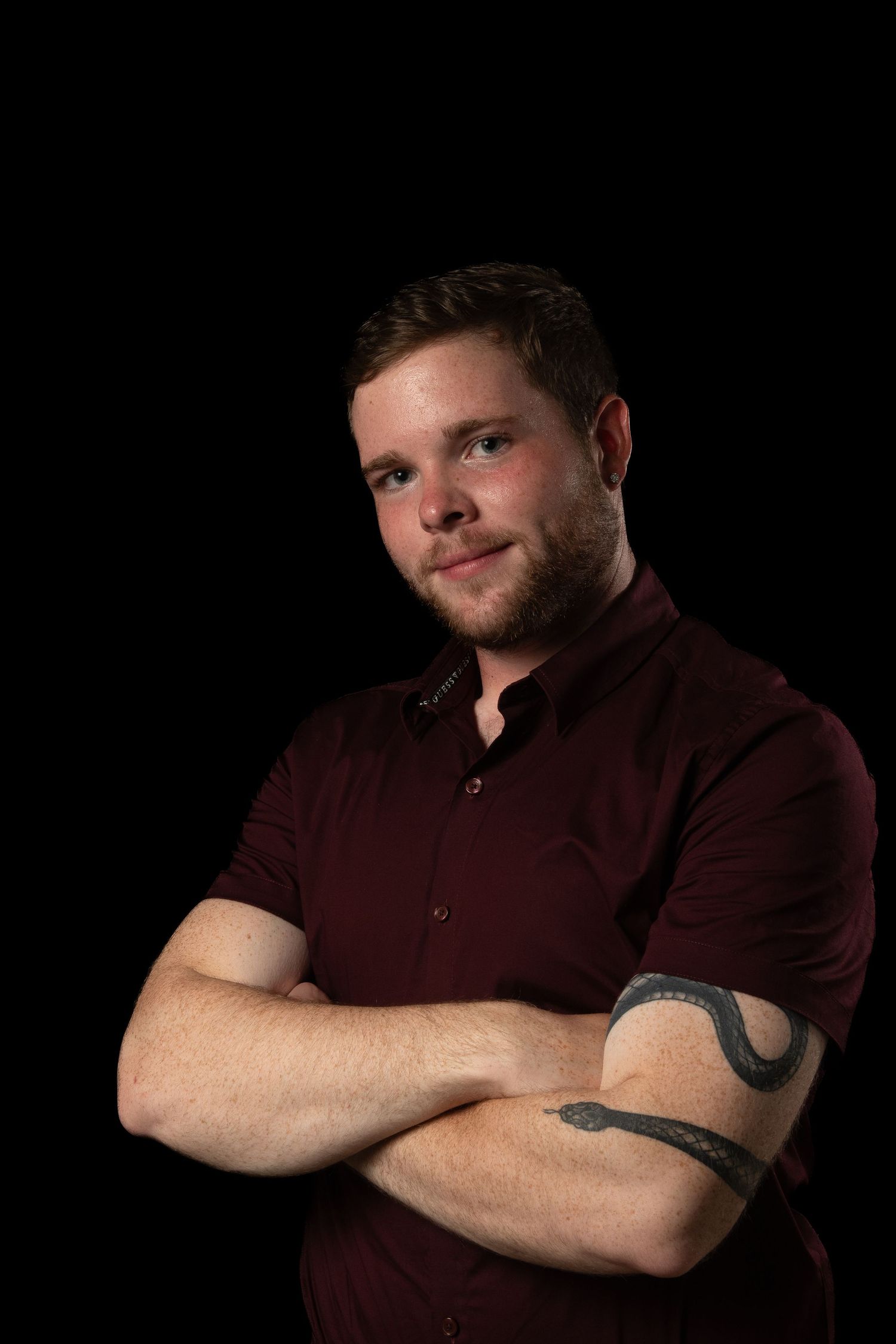 Professional portrait against black background showing thoughtful expression in burgundy shirt.