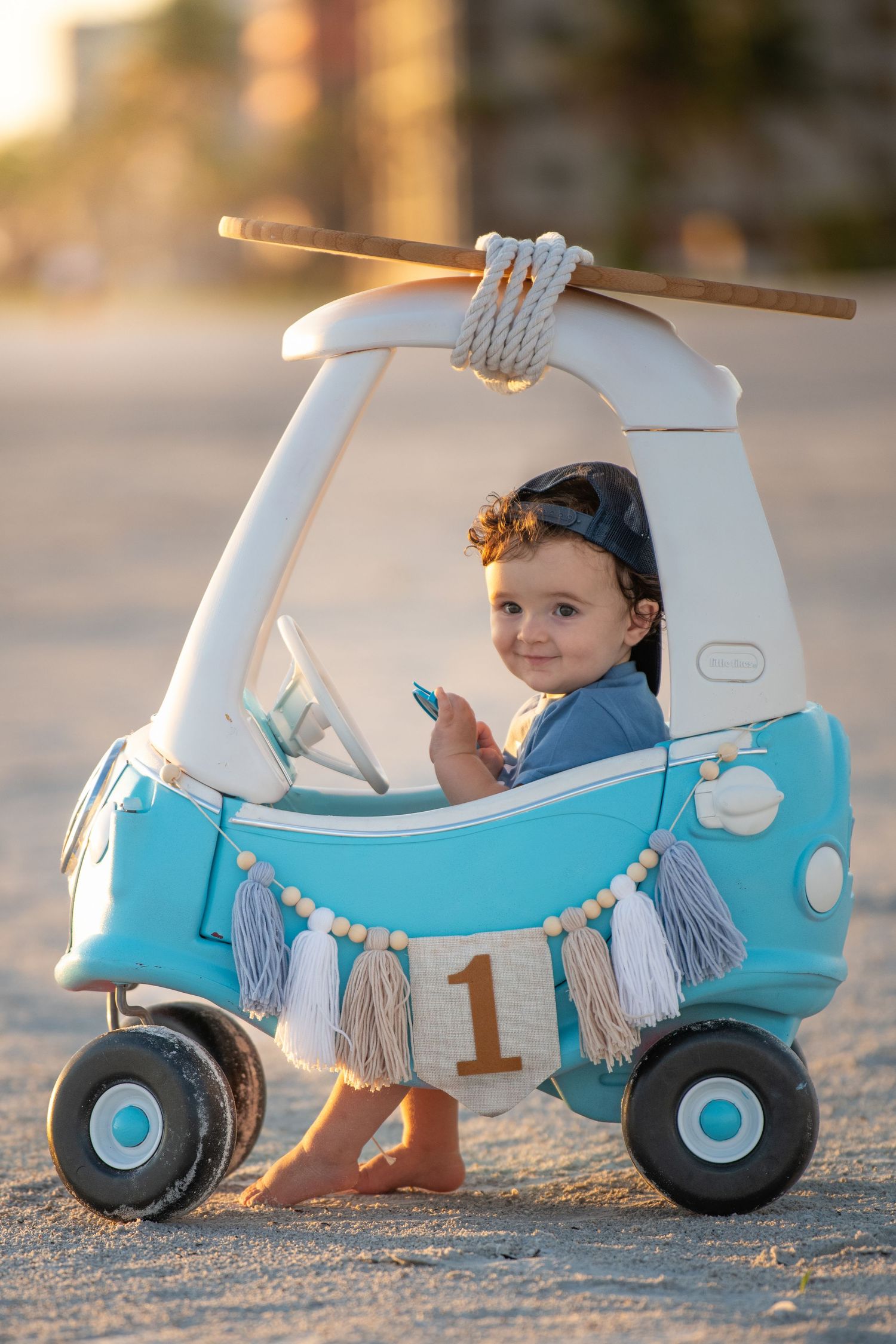 Light blue toy car with decorative banner on beach sand.