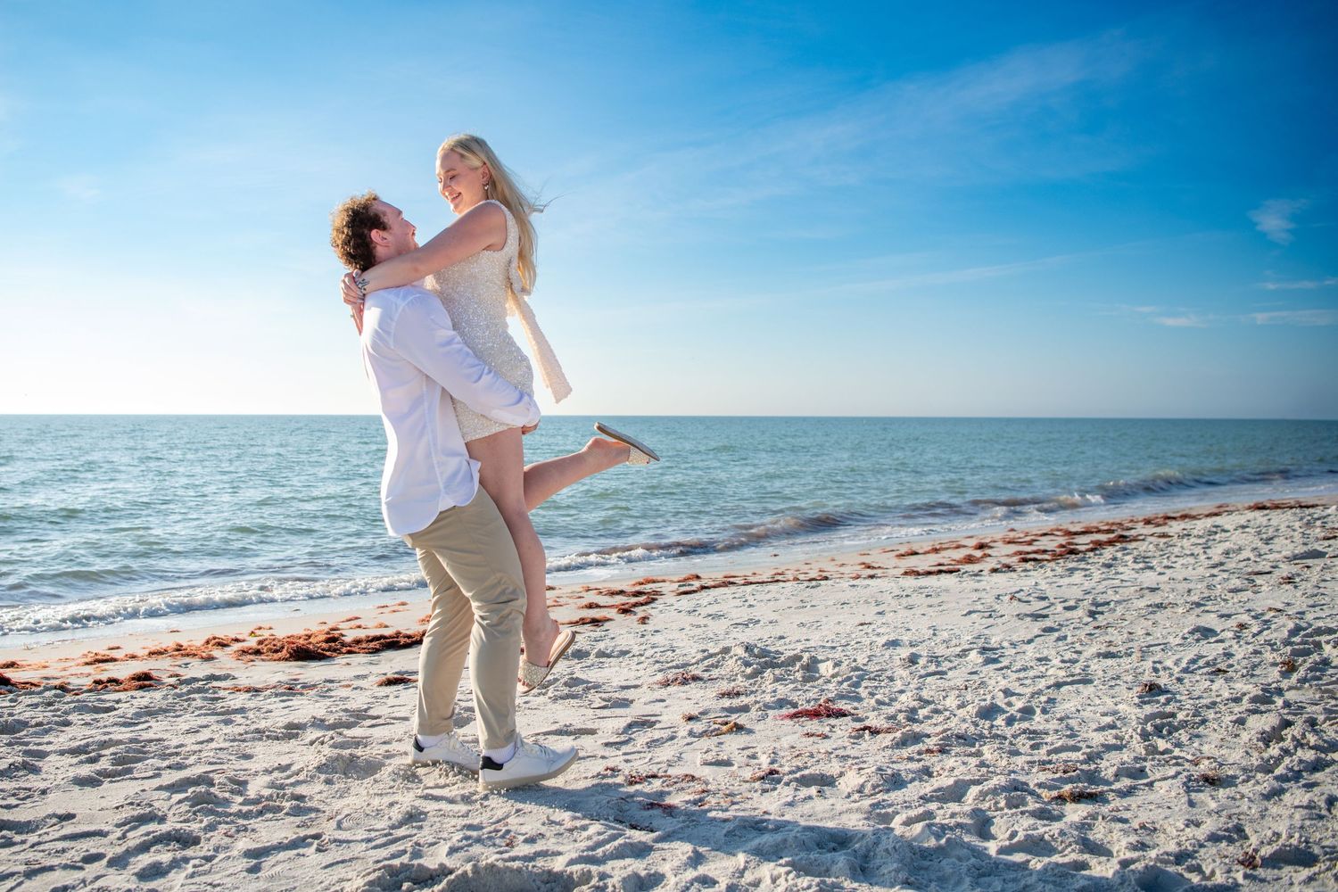Playful beach engagement photos with a couple dancing and embracing on white sand. Engagement photoshoot. Couples photos.
