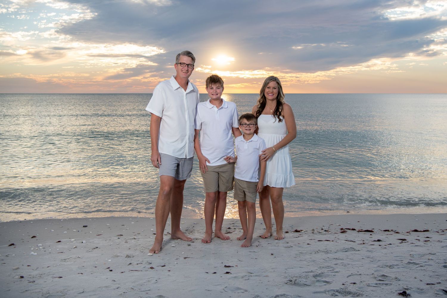 Family portrait session on sandy beach with golden sunset sky and calm ocean waters. Beach photoshoot. Family photoshoot,