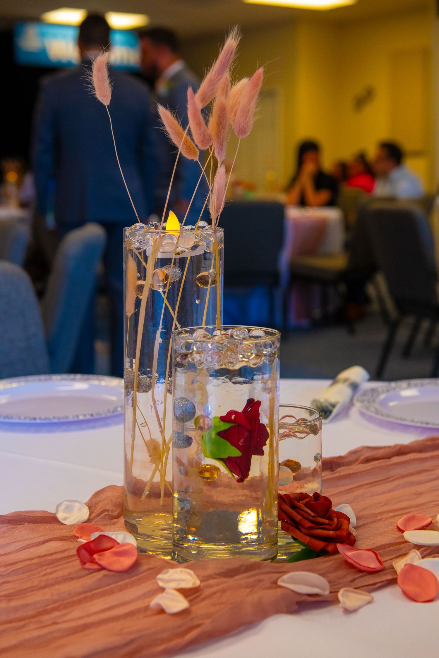 Wedding table centerpieces with glass vases, roses, and decorative elements on a striped runner.