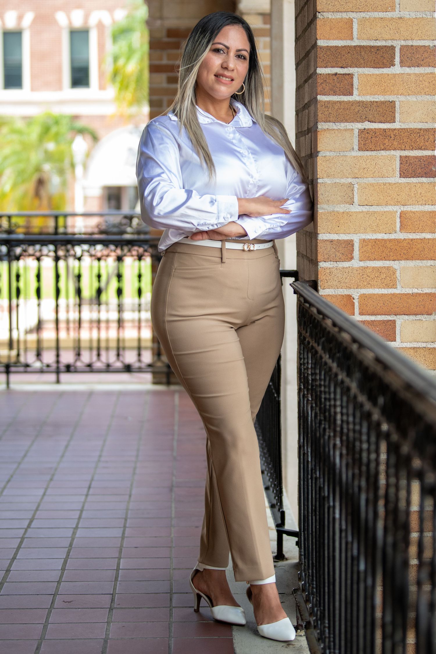 Professional wearing crisp white button-down shirt and khaki pants poses confidently against brick wall.