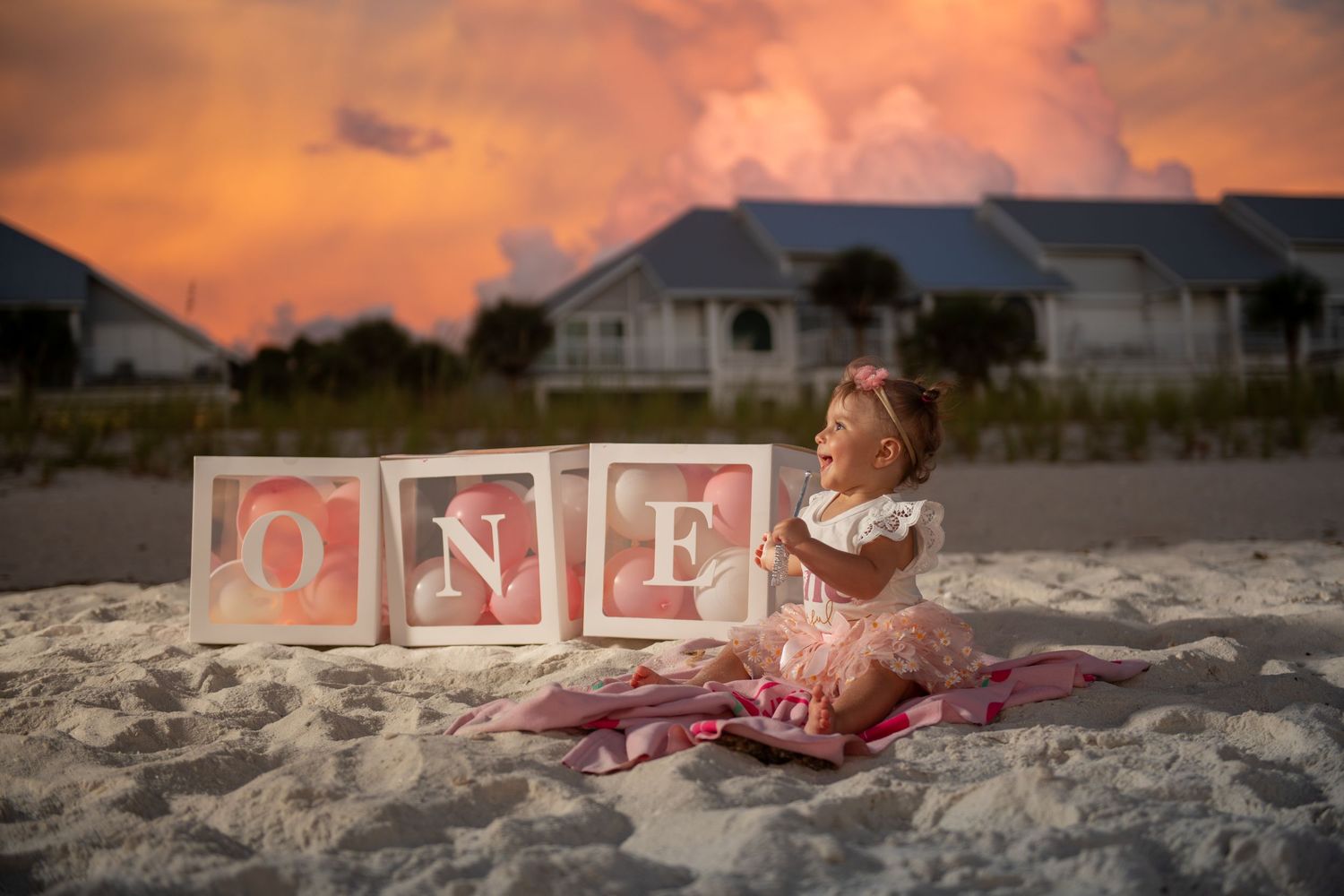 Pink and white letter blocks spell out 'ONE' on a sandy beach at sunset.