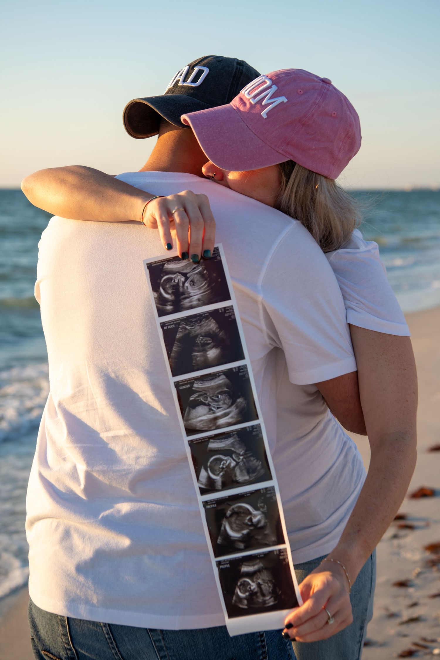Couple displays ultrasound photos on beach during sunset maternity shoot. Maternity photoshoot. Couples photos.