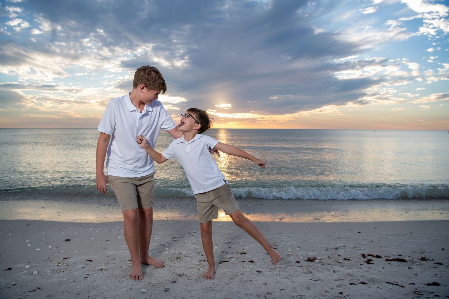 Playful beach photography session with white-clad figures against dramatic sunset sky. Beach photoshoot. Family photoshoot,