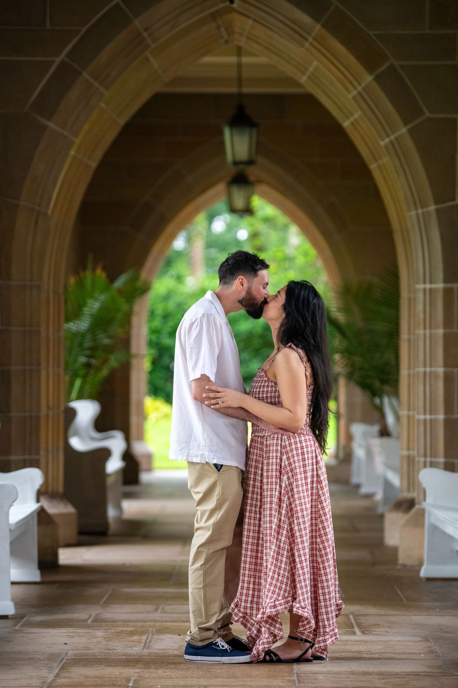 A couple shares intimate moments under a beautiful stone archway walkway with natural lighting.