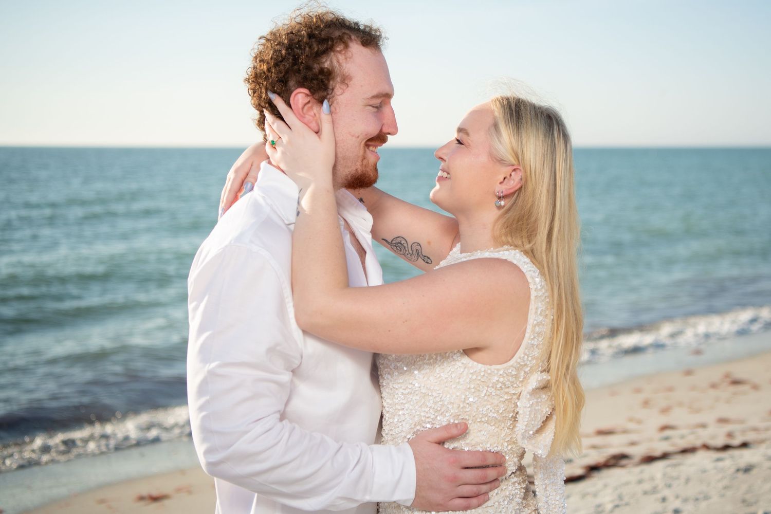 A joyful embrace between a newly engaged couple on a sunny beach with ocean waves behind them. Engagement photoshoot. Couples photos.
