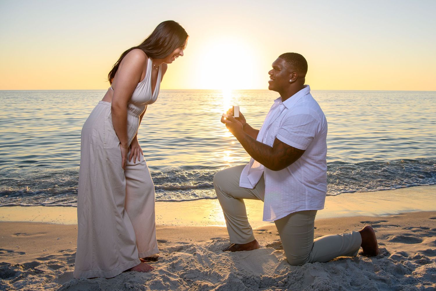 Romantic beach proposal scene with couple in white and khaki at golden hour. Engagement photoshoot. Couples photos.