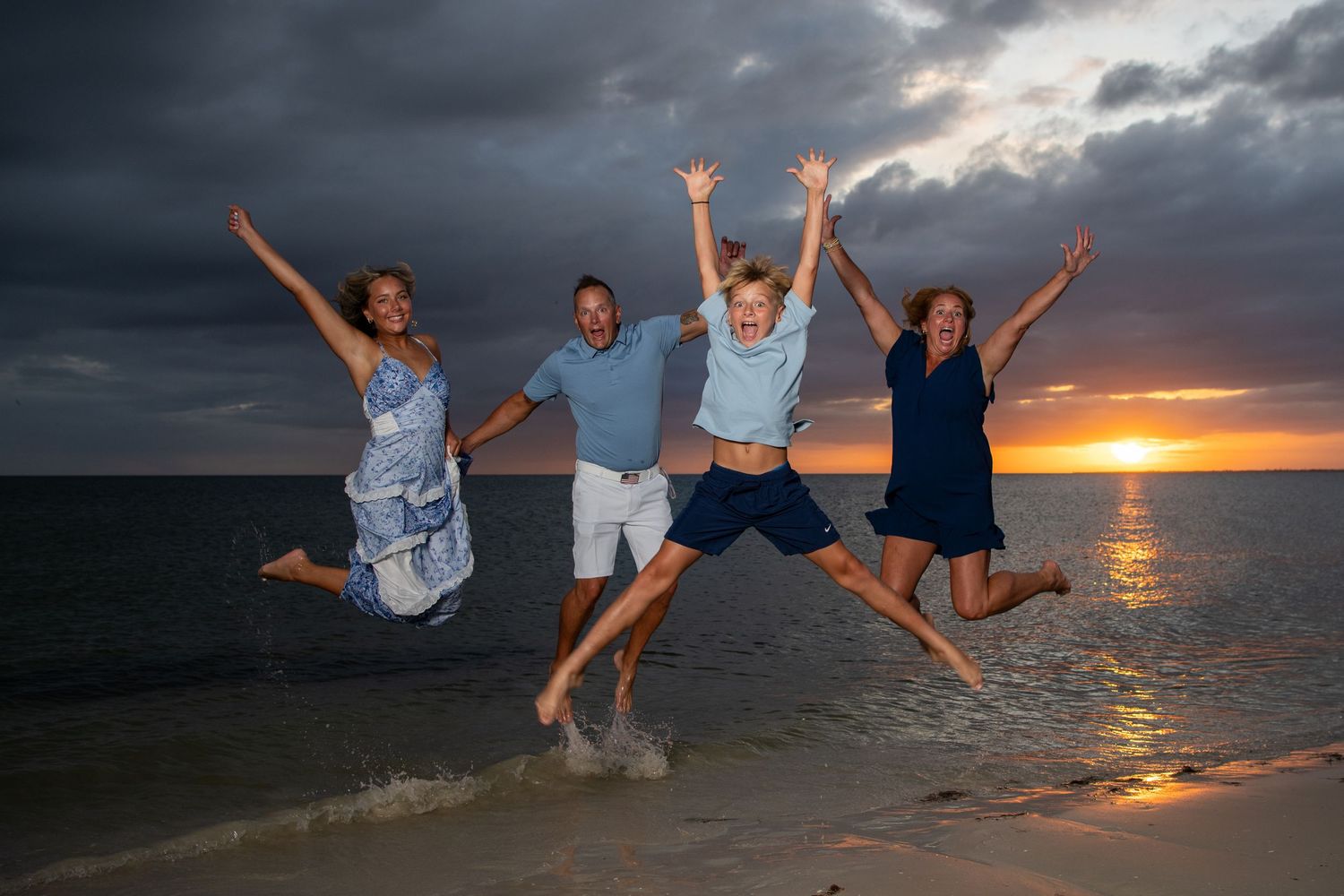 Group jumping playfully on beach at sunset with dramatic cloudy sky. Beach photoshoot. Family photoshoot,